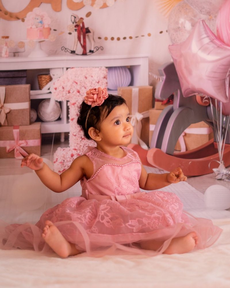 A baby girl in a pink dress sitting on a soft rug