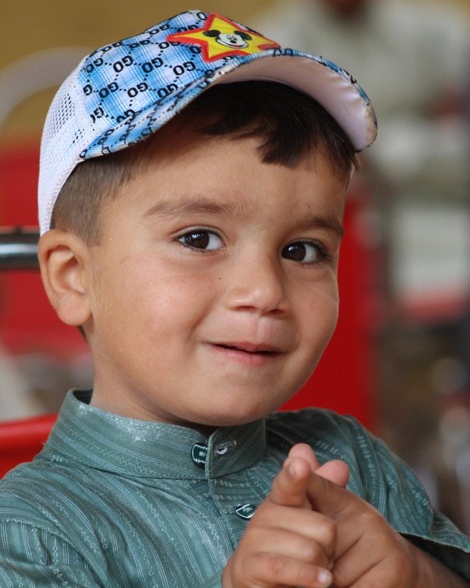 A smiling little boy in a cap, pointing at the camera