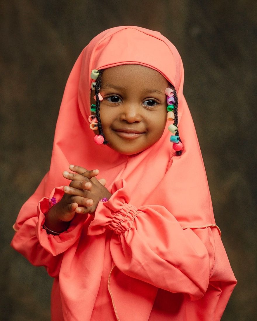 A smiling little girl in a coral dress and hijab