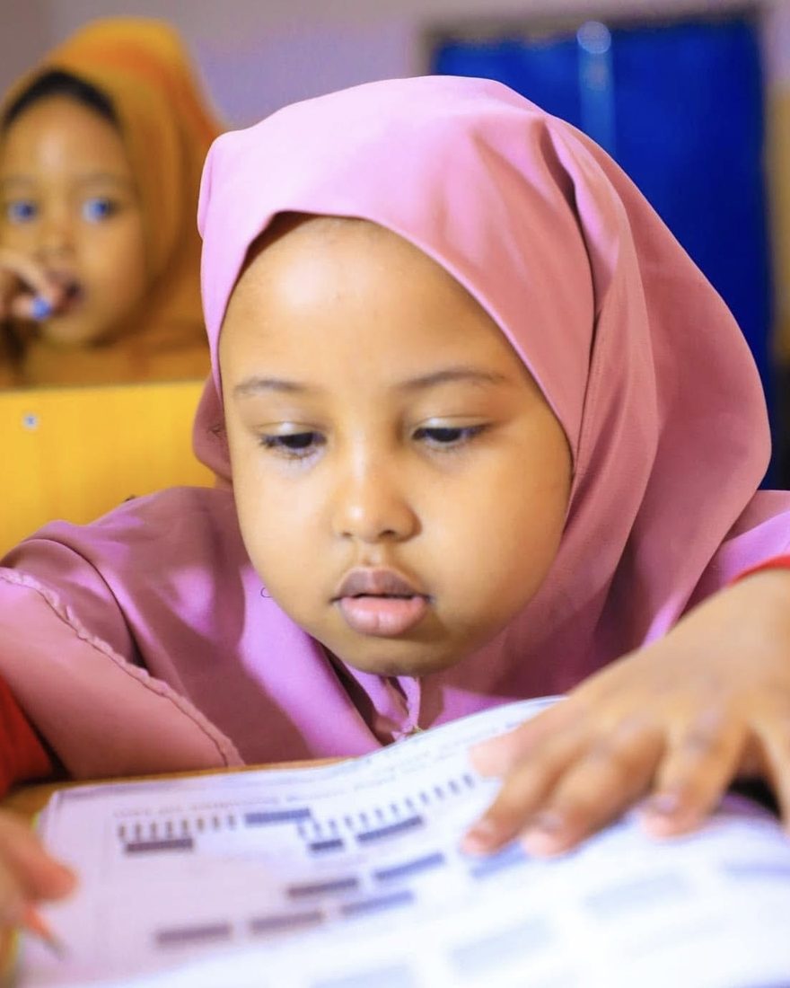A girl in a pink hijab working on a worksheet