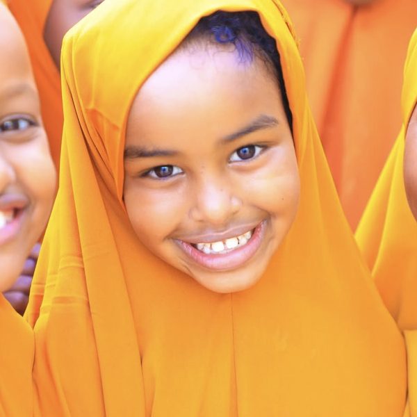 A smiling girl in an orange hijab with her friends
